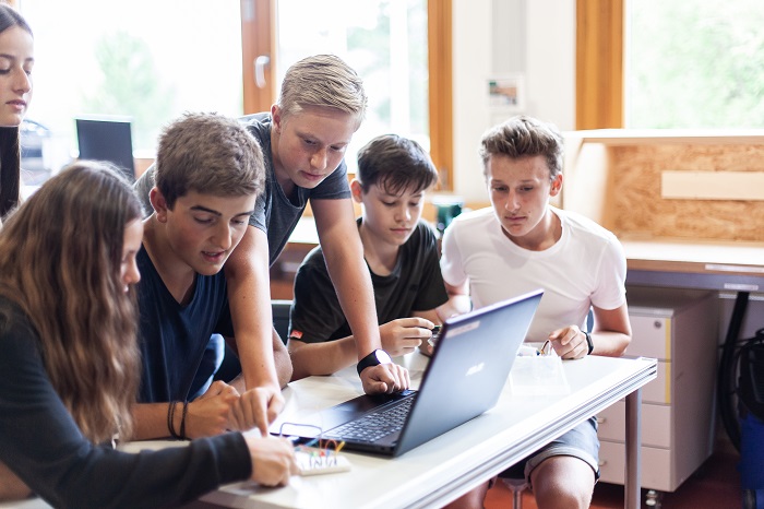 Eine Gruppe an Schülerinnen und Schüler sitzen um einen Laptop herum und brainstormen.