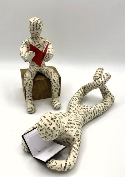 Figuren aus Buchseitenpapier, welche liegend und sitzend lesen von Moritz Kammerer (10b) & Tiala Herzog (10b), Januar 2025.